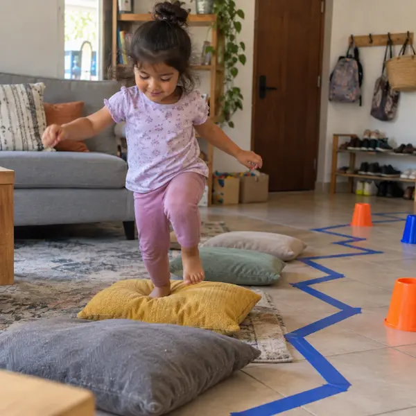 Niña saltando sobre cojines en un circuito de movimiento en la sala